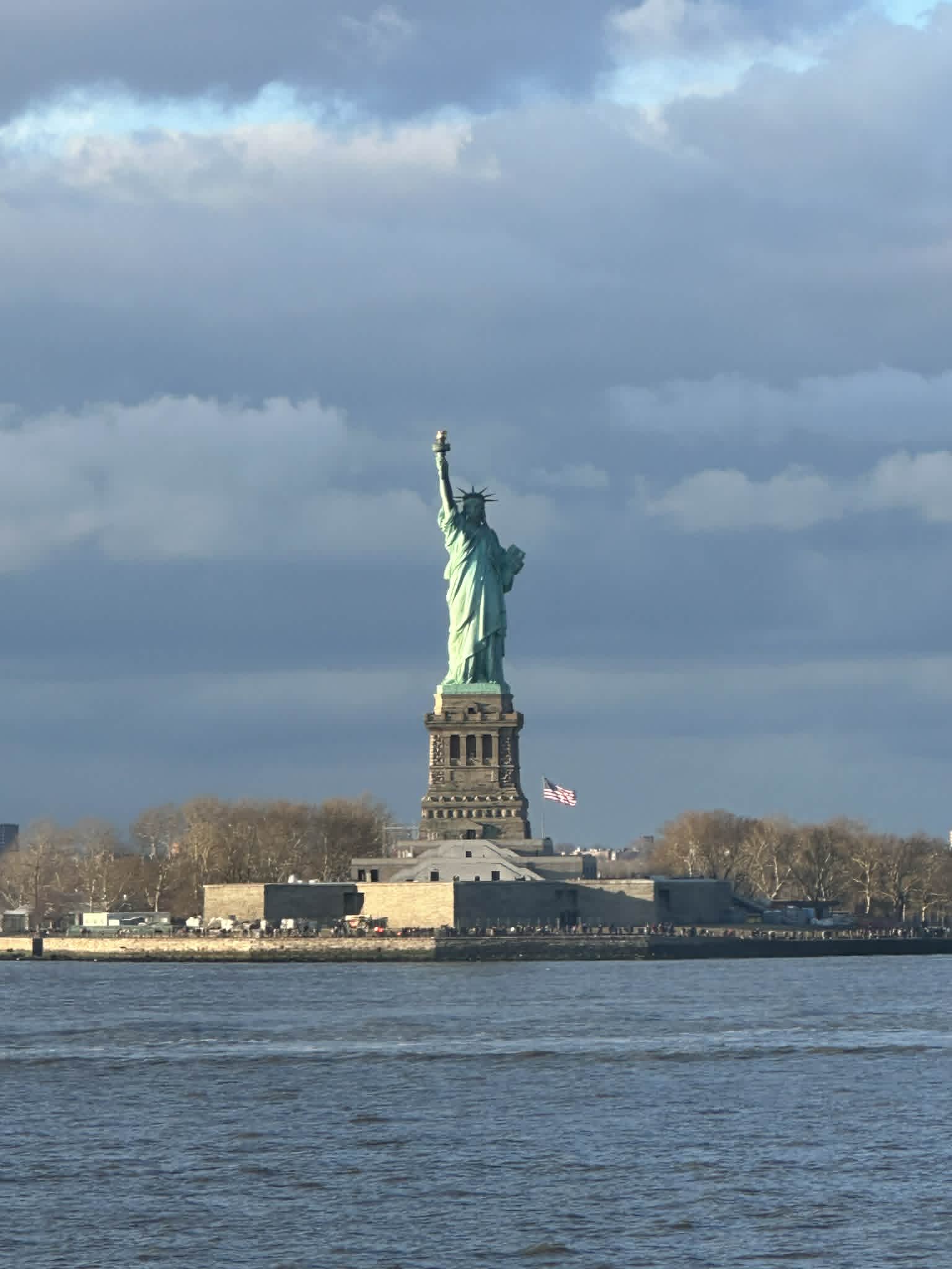 The Statue of Liberty viewed from the Staten Island ferry on a cloudy winter day, with the American flag visible at the base
