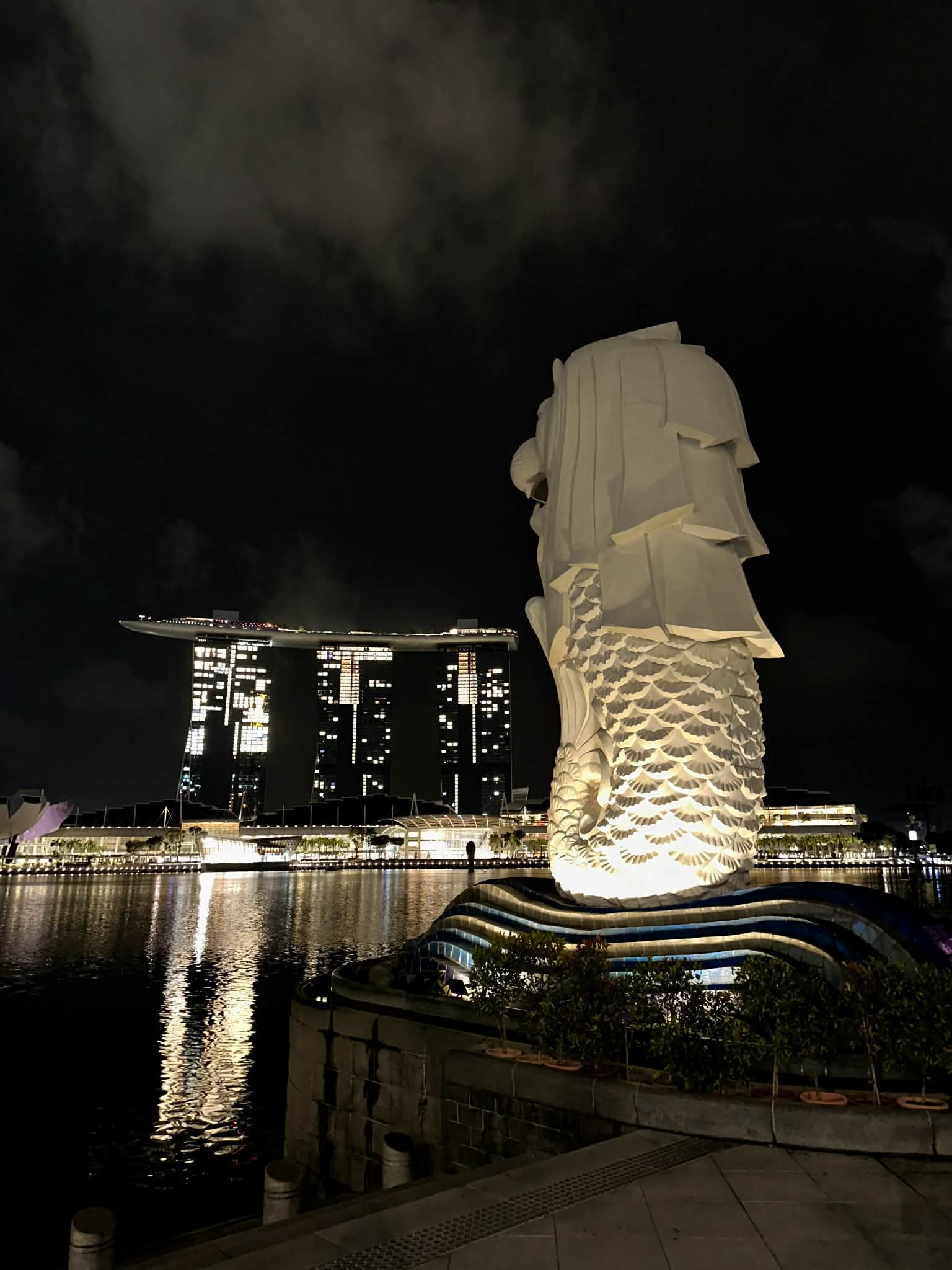The Merlion statue at Marina Bay illuminated at night, water spouting from its mouth into the harbour